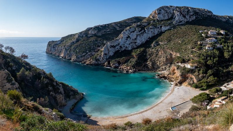 Een baai van Jávea omringd door kliffen en pijnbomen.
