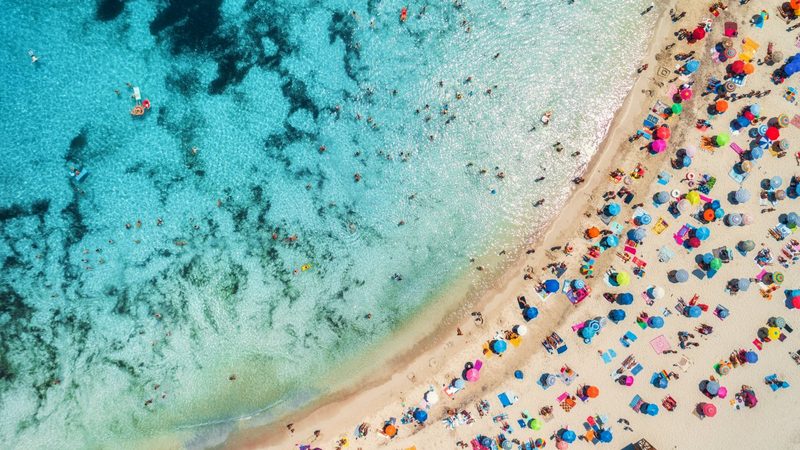 Een strand aan de Costa Blanca vanuit de lucht, met parasols op een rij in het zand.
